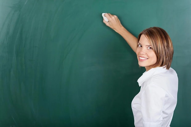 Smiling female teacher holding a chalk and writing on the blackboard